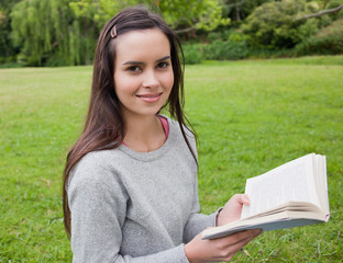Smiling young girl standing upright in the countryside while rea