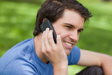 Smiling young man sitting in the countryside while using his cel