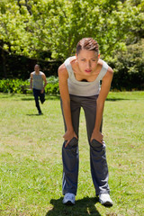 woman bending over while a man is running in the background