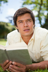 Man looks to the distance while reading a book as he is lying do