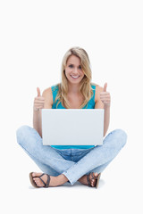 A woman with her thumbs up is sitting on the ground with a lapto