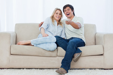 A young couple are sitting down looking at the camera and laughi