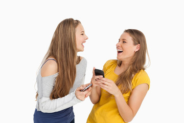 Two young women laughing while holding their cellphones