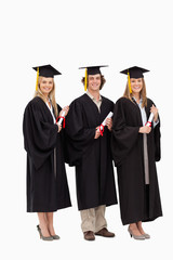 Three smiling students in graduate robe holding a diploma