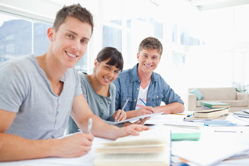 Fototapeta premium Three smiling students doing homework as they look into the came