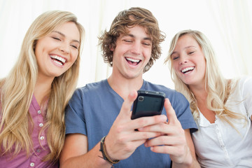 Three friends looking at the screen of a mobile phone while smil