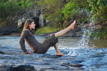 Fröhliche junge Frau spritzt Wasser mit dem Fuß