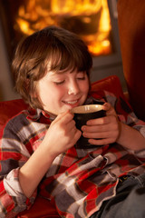 Young Boy Relaxing With Hot Drink By Cosy Log Fire