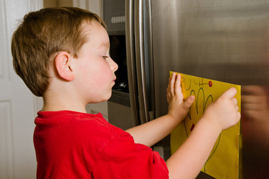 Child putting his art up on family refrigerator at home