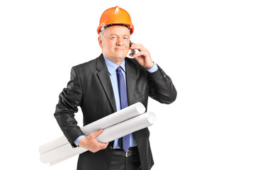 Mature construction worker holding blueprints and talking on a p