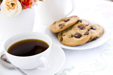 Chocolate chip cookie  on white plate with black coffee and flow