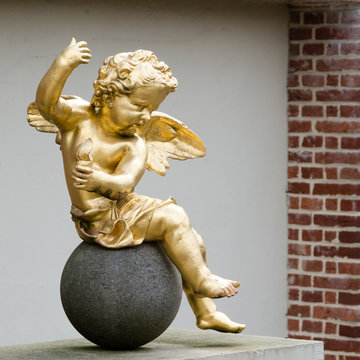 A golden putto sitting on a round stone
