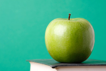 A green apple over a book on green background