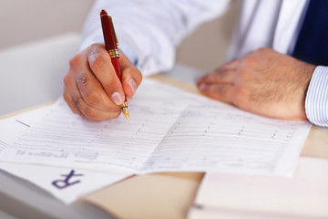 Hands of a doctor filling RX prescription, documents at the desk