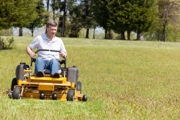 Senior man on zero turn lawn mower on turf