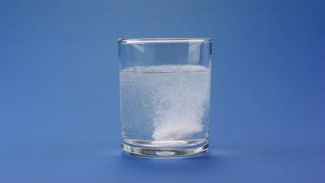 effervescent pill dropping into a glass of water over blue
