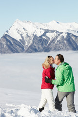 Fototapeta na wymiar Couple Admiring Mountain View Whilst On Ski Holiday In Mountains