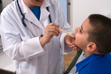 Doctor checking throat of a little boy with tongue depressor
