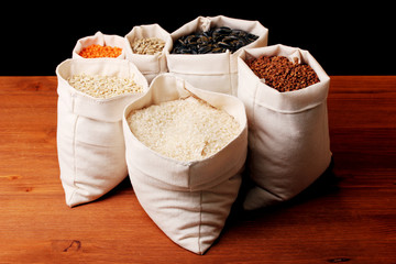 Cloth bags with grain on wooden table on brown background