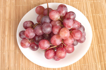 Red grape berries branch in white round plate on straw surface