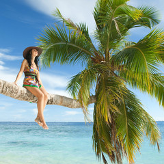 Fashion woman siting upon palm tree on the beach