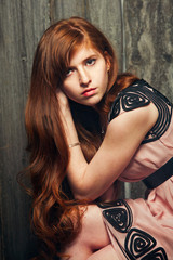Fototapeta na wymiar Beautiful sensual red-haired girl standing near a wooden wall