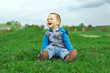 happy laughing baby boy sitting on green field