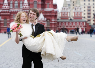 Happy groom holding young beautiful bride in his arms