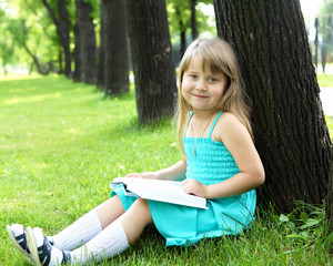 Portrait of little girl reading a book in the park