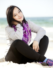 Fototapeta na wymiar Funny teen girl sitting on the sand at the beach.