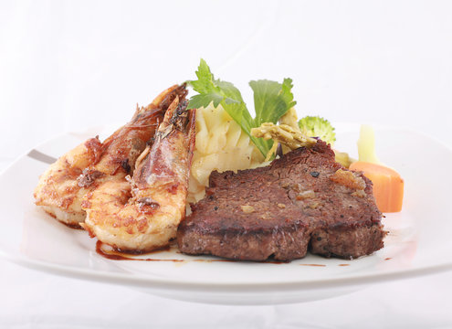 A steak and shrimp dinner over a plaid tablecloth
