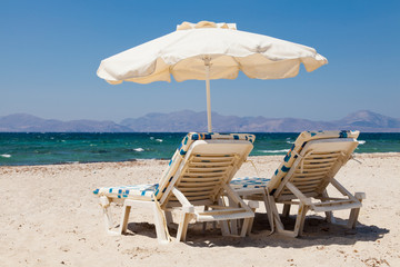 Deckchairs under parasol on sunny beach