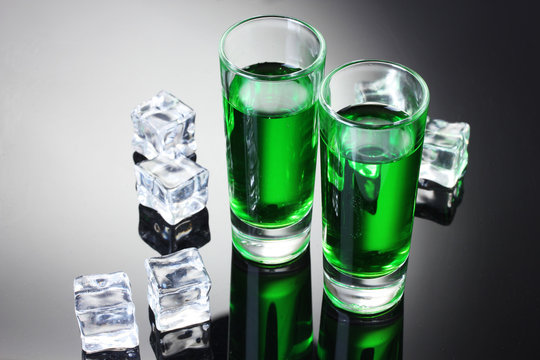 Two glasses of absinthe and ice on grey background