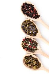Different dry green and black tea in wooden spoons isolated