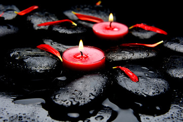 Two red candle red petals with wet black stones