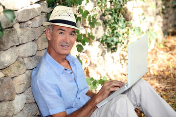 Man with computer leaning on stone wall
