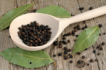 Black pepper in spoon and dry bay leaf on wooden background