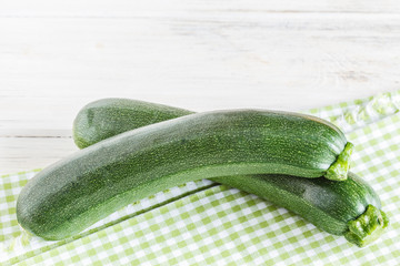 Zucchini mit karierter Serviette auf weißem Holzuntergrund.
