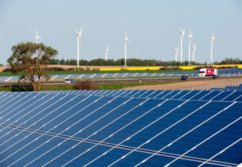 Windkrafträder und Solarmodule in einem Rapsfeld