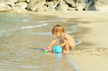 Happy toddler girl playing with her bucket at the beach