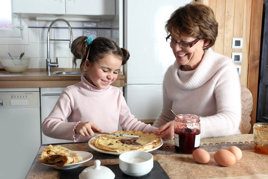 Young girl preparing crepes with her grandmother