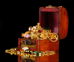 Wooden chest full of gold jewelry on black background