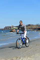 Fototapeta premium Portrait of handsome male riding a bicycle by the sea