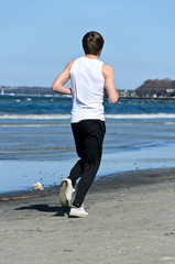 Athletic young male running on the beach. From the back