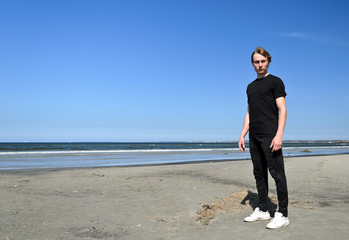 Young male in black clothes standing on the beach