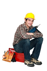 young craftsman holding a drill and sitting on a tool box