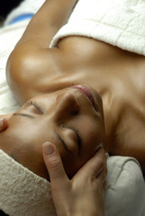 Joven mujer morena recibiendo masaje facial en un spa.