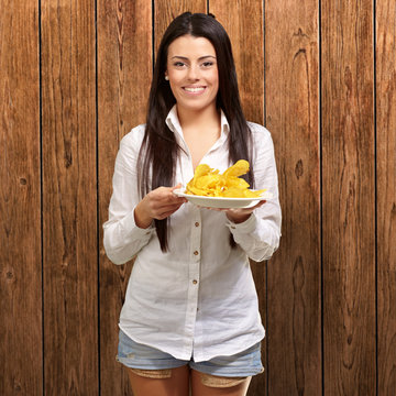 portrait of young woman holding a potato chips plate against a w