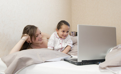 Fille et sa mère dans le lit devant l'ordinateur