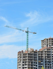 Fototapeta premium Building crane and building under construction against blue sky